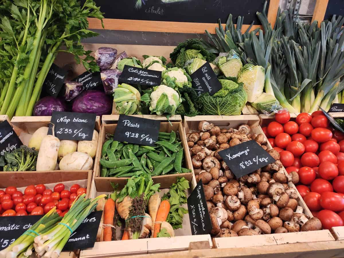 An image of various different vegetables in boxes in a fruit shop. Each vegetable is labelled and priced.