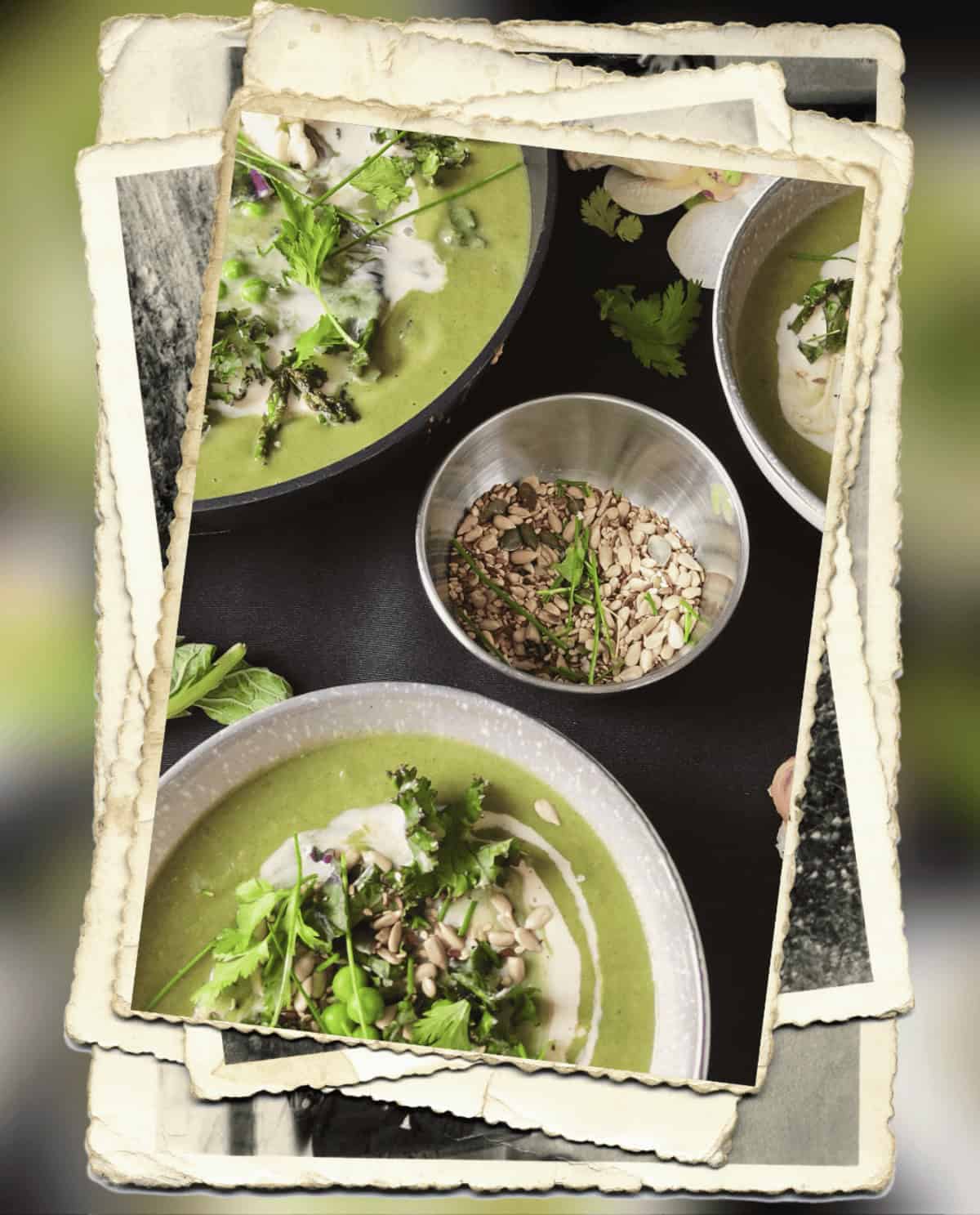 A vibrant green soup served in bowls, garnished with fresh herbs, a drizzle of cream, and sprinkled with seeds. A metal bowl filled with mixed seeds is placed in the center, surrounded by additional bowls of the soup on a dark background. The image has a layered vintage photo frame effect.