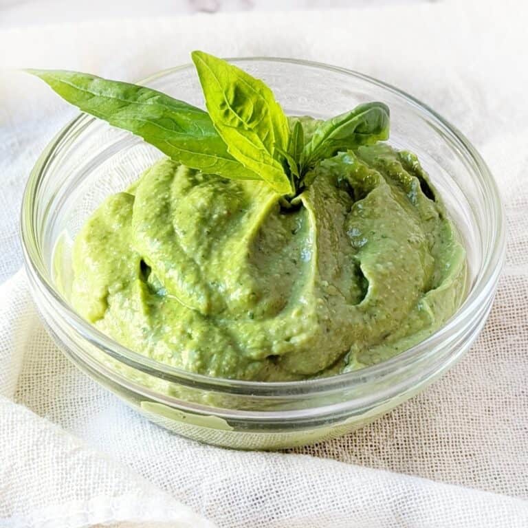 A small glass bowl of creamy chili avocado pesto with a basil leave on the top