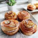 Beautiful puff pastry apple roses dusted with powdered sugar, elegantly displayed on a striped plate with a succulent plant in the background.