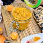 Jar of homemade níspero (loquat) chutney with fresh loquats and Indian spices on a rustic wooden board.