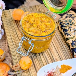 Jar of homemade níspero (loquat) chutney with fresh loquats and Indian spices on a rustic wooden board.