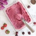 A scoop of ice cream in a bowl with cherries and strawberries.Chocolate shavings in the background.