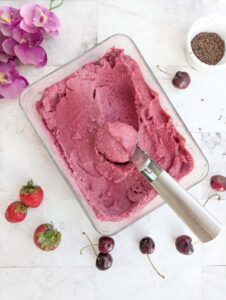A scoop of ice cream in a bowl with cherries and strawberries.Chocolate shavings in the background.
