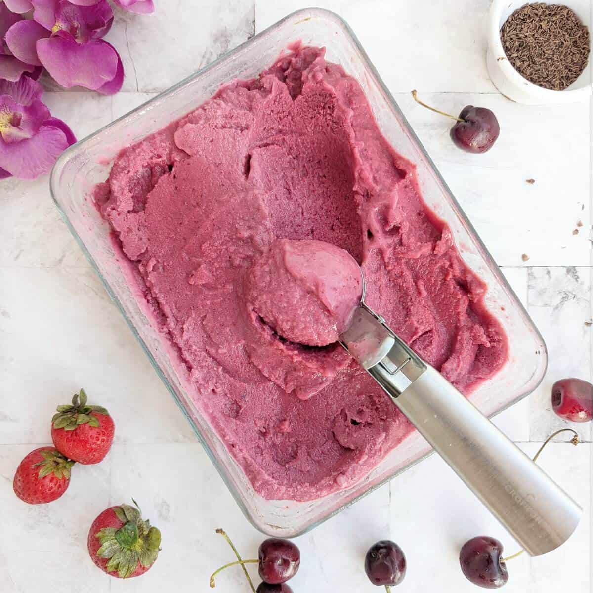 A scoop of vegan ice cream in a bowl with cherries and strawberries.Chocolate shavings in the background.