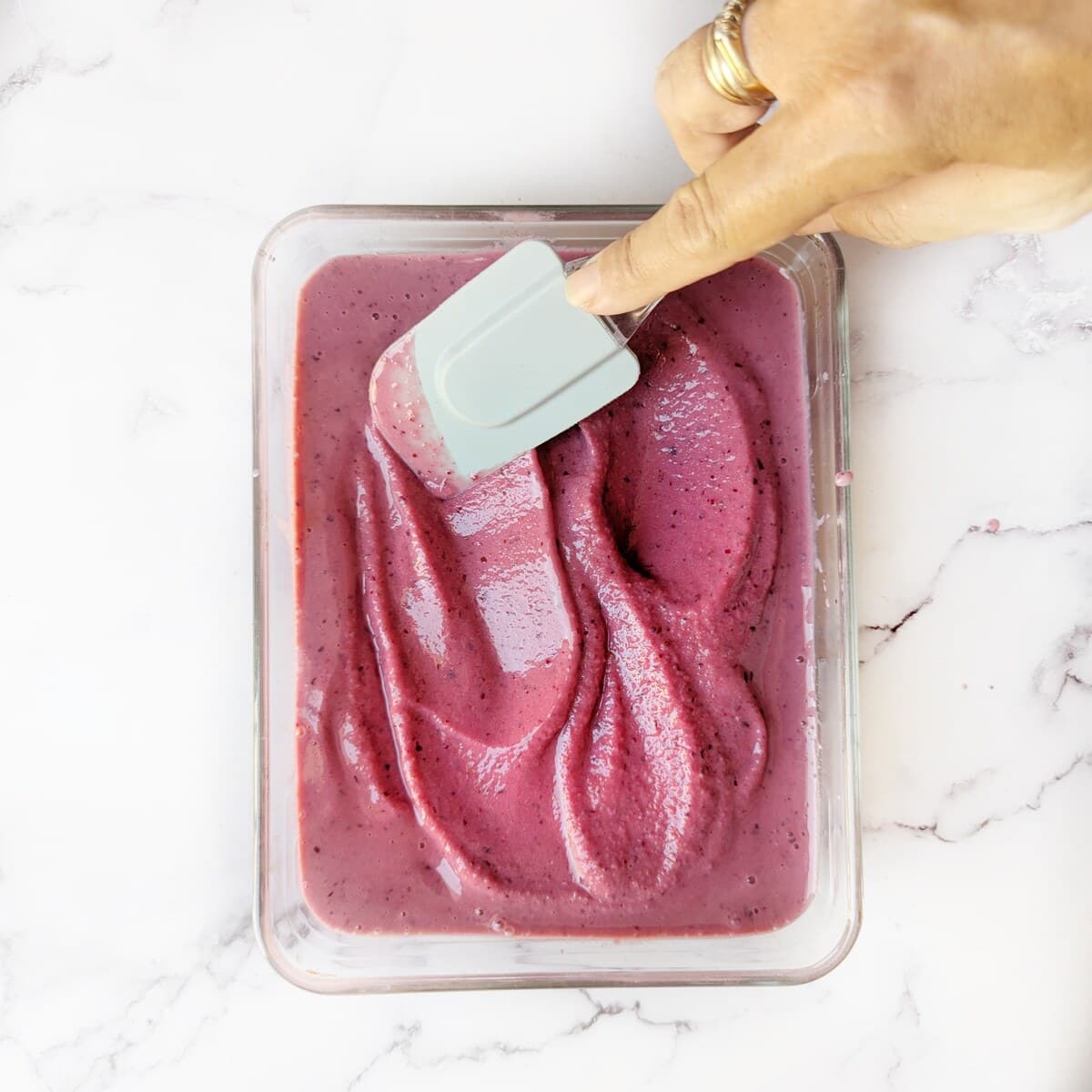 A person using a spatula to mix the berry ice cream.