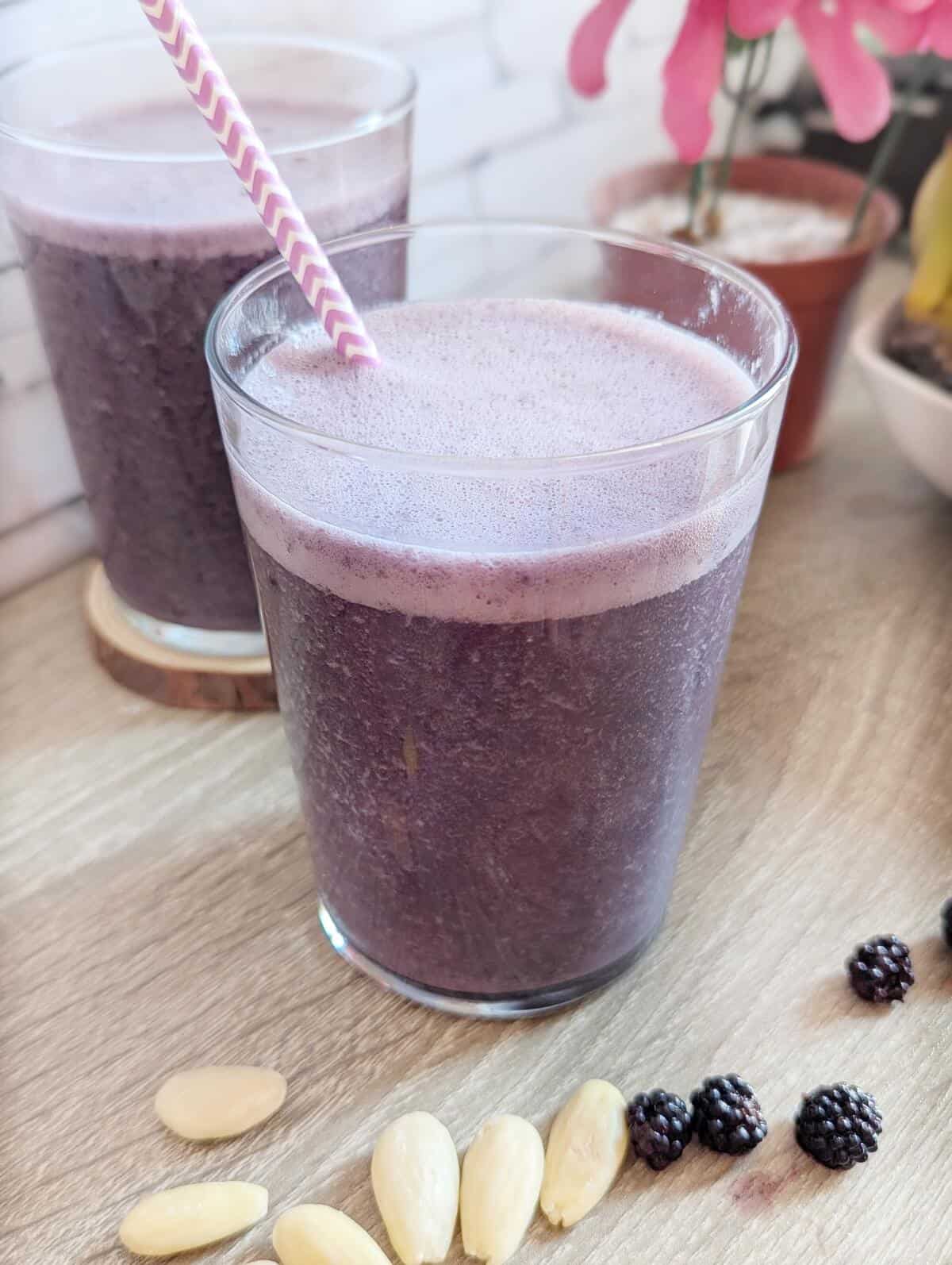 Two glasses of blackberry smoothie, almonds and blackberries lying in front.