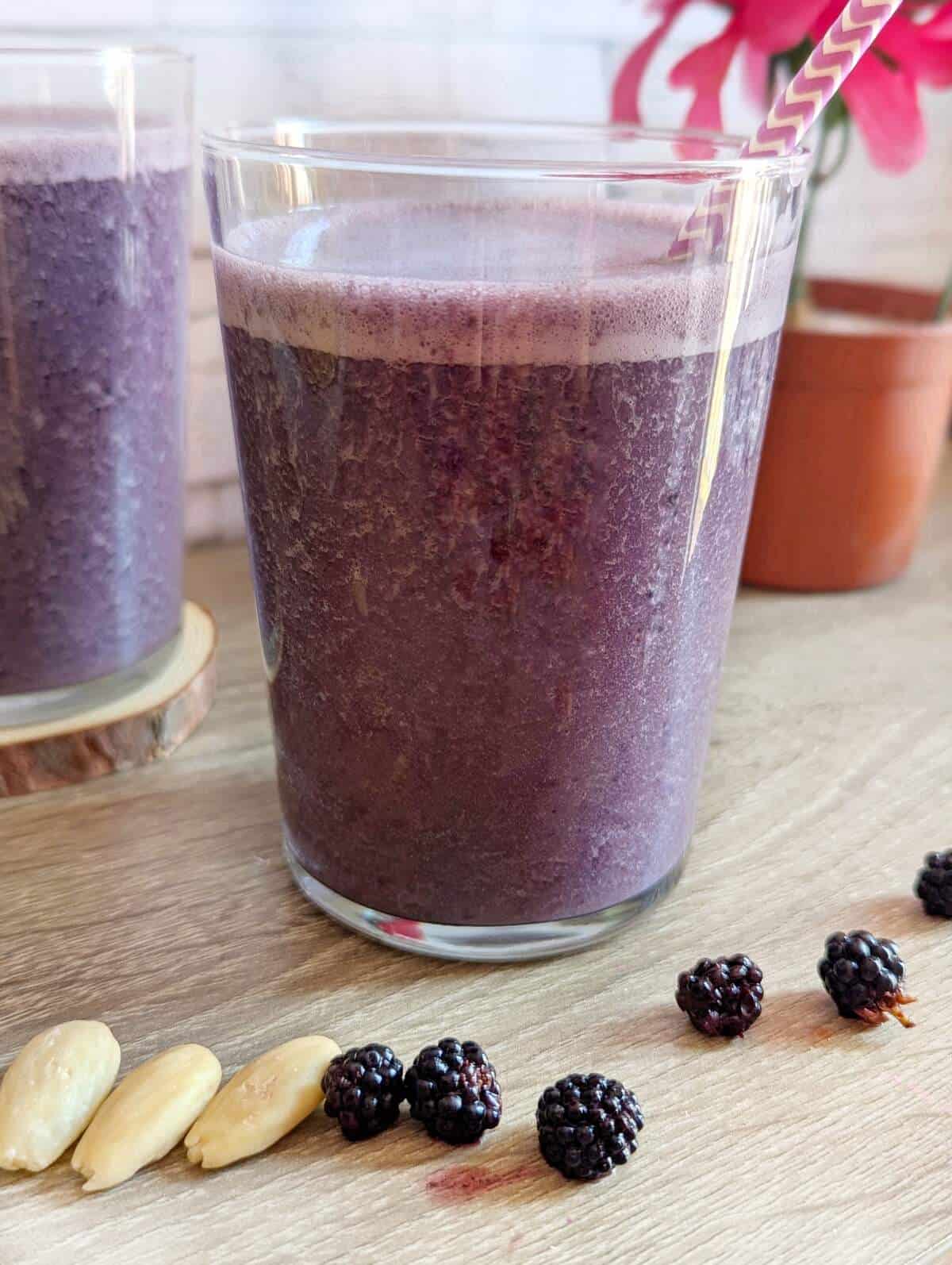 A close uo glass of blackberry banana smoothie with almonds.