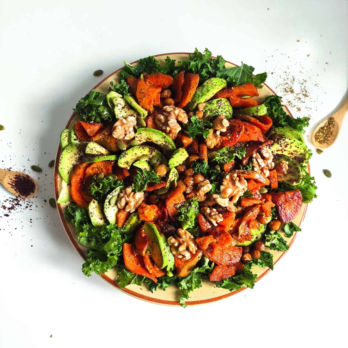 A plate of roasted squash, sweet potato, chickpeas, avocado, walnuts and kale.