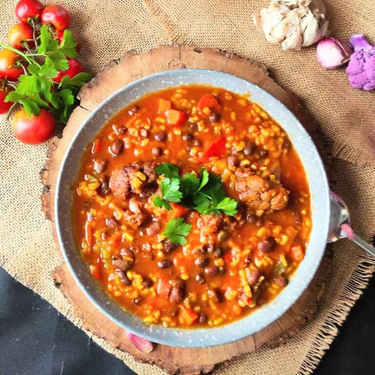 A bowl of adzuki bean stew with tomotoes, garlic and purple cauliflower in the background.