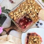 A dish displaying chia berry oat crumble with a plate showing a portion of it.