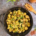A skillet filled with brussels sprouts and herbs. A wooden spoon by the side and chili flakes.