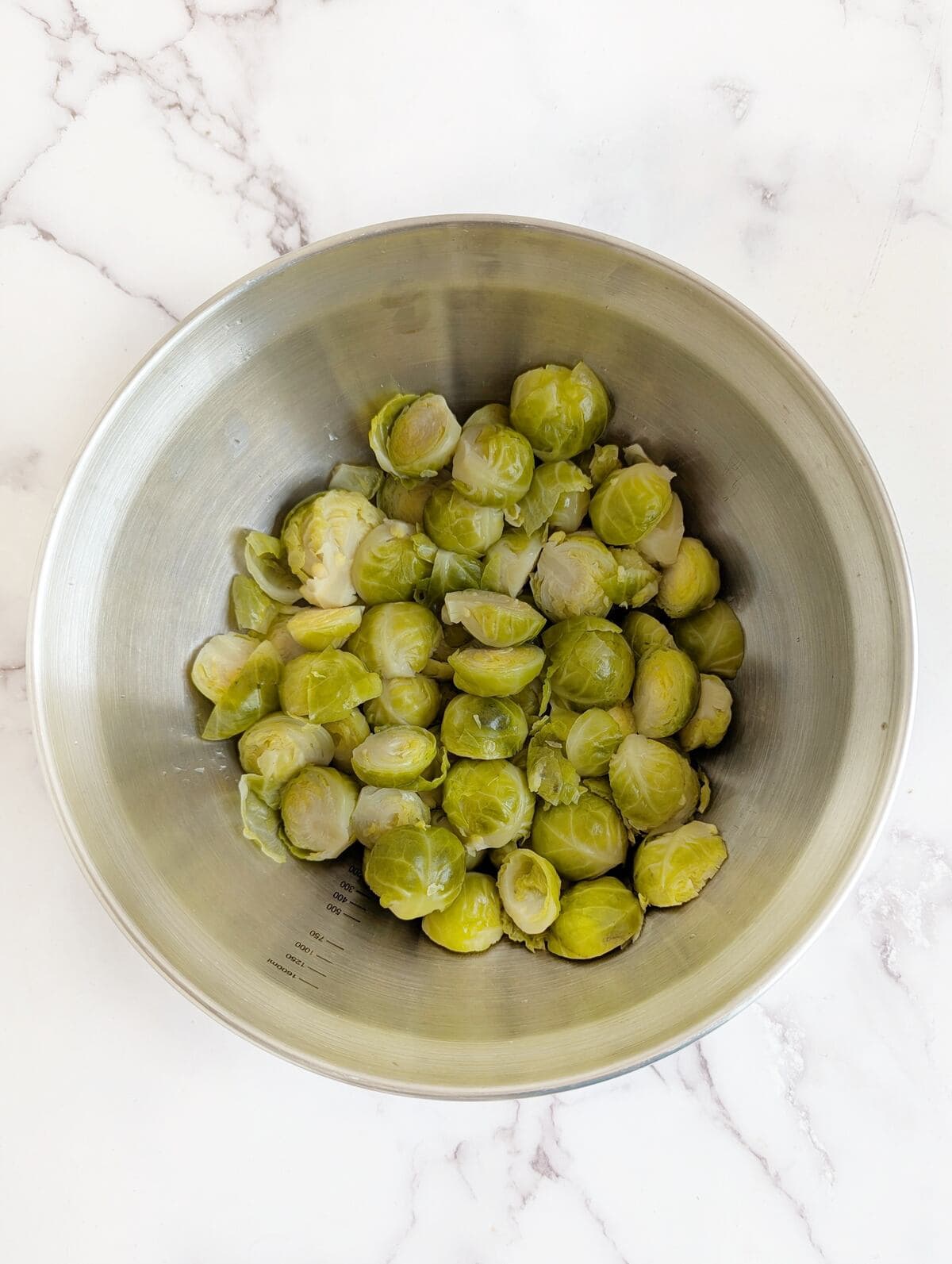 A bowl filled with brussels sprouts on a marble surface.