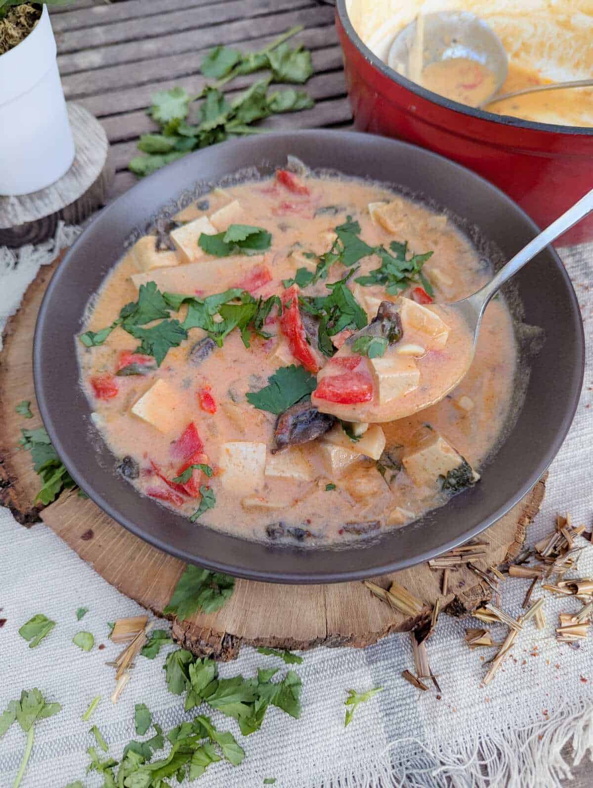 A bowl of creamy Thai soup with tofu, lemongrass and cilantro is sprinkled infront of the bowl.