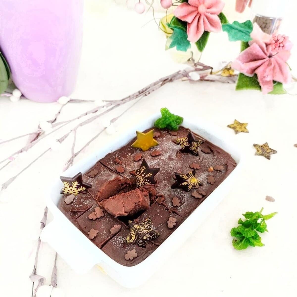 Vegan chocolate fudge topped with decorative stars and sprinkles, styled on a white plate with pink flowers and greenery.