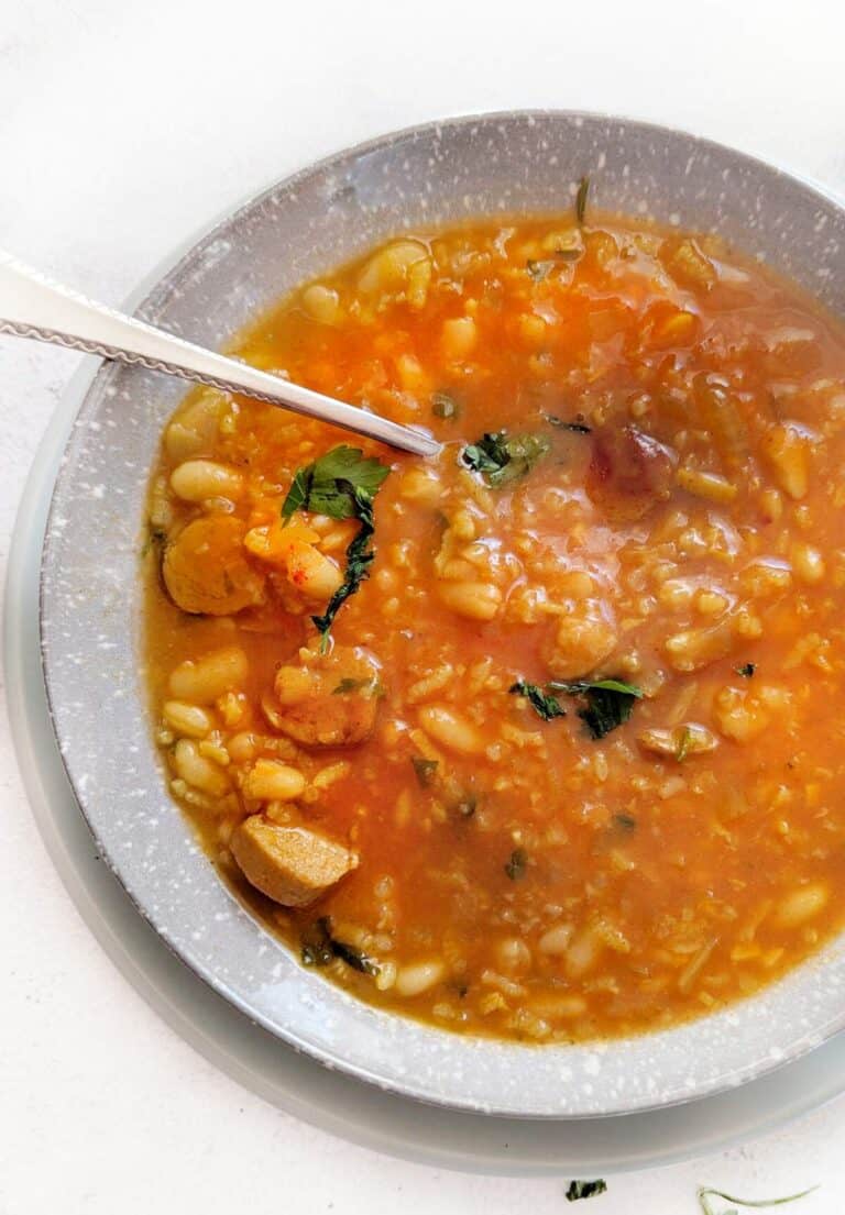 An image of half a bowl of sausage bean soup with a spoon in it.