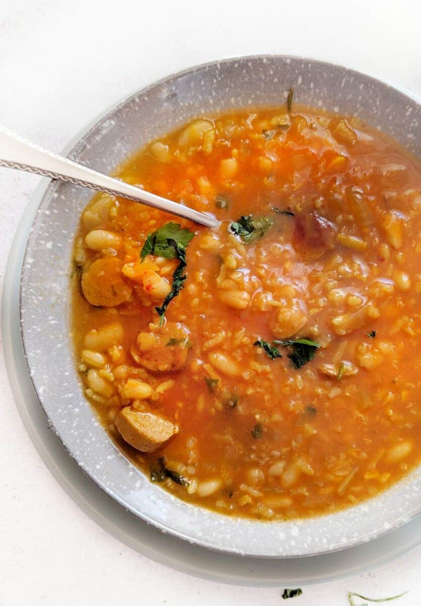 An image of half a bowl of sausage bean soup with a spoon in it.