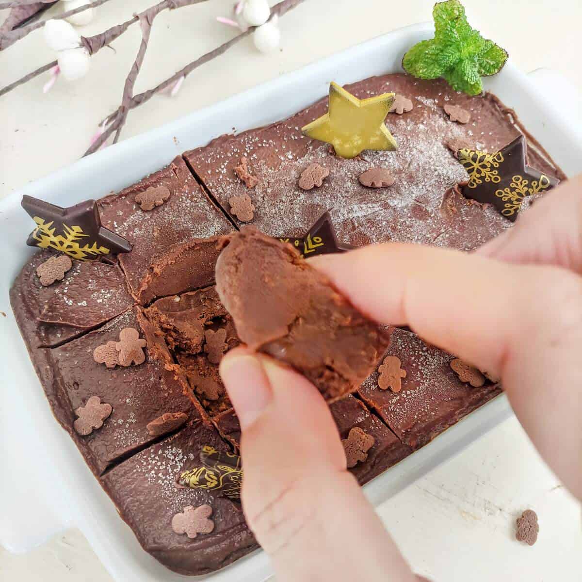 A close up image of chocolate mint fudge with pretty chocolate stars on top. A hand is holding a slice.
