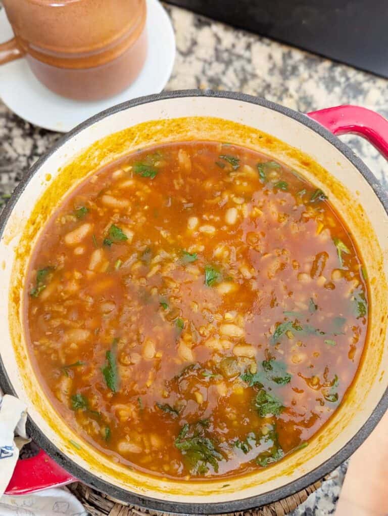 A pot of vegan sausage bean and rice soup. A rustic pot is behind the pot.
