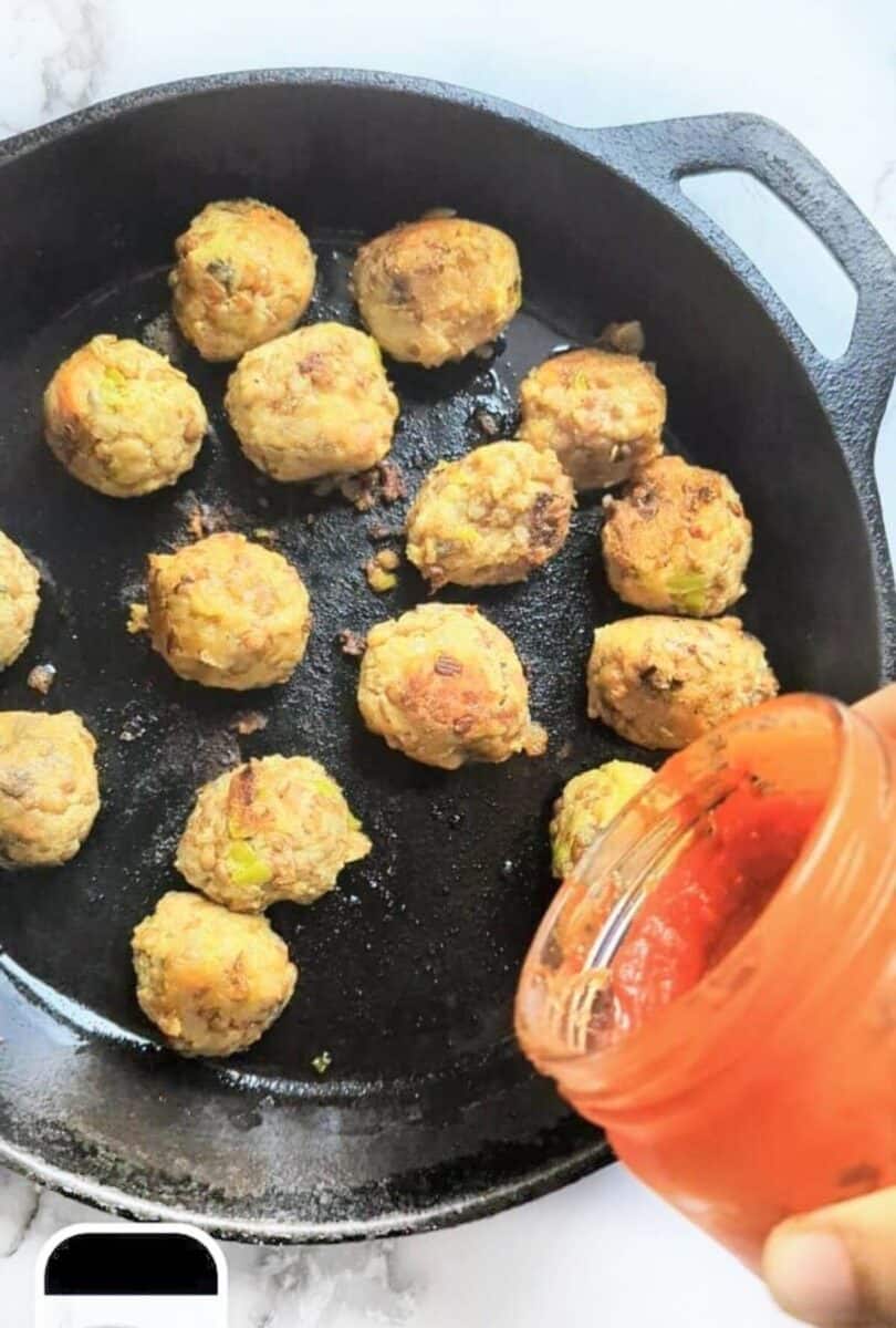 Tomato sauce being added to the pan of vegan meatballs.