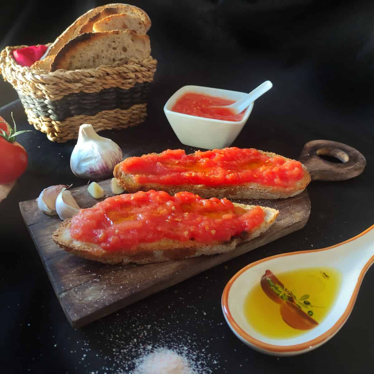 Toasted sourdough garlic bread on a wooden board, topped with fresh tomato and olive oil.