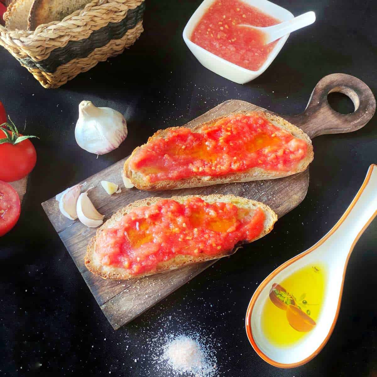 Toasted garlic bread on a wooden board, topped with fresh tomato and olive oil. A typical Spanish breakfast. A garlic clove in the background.
