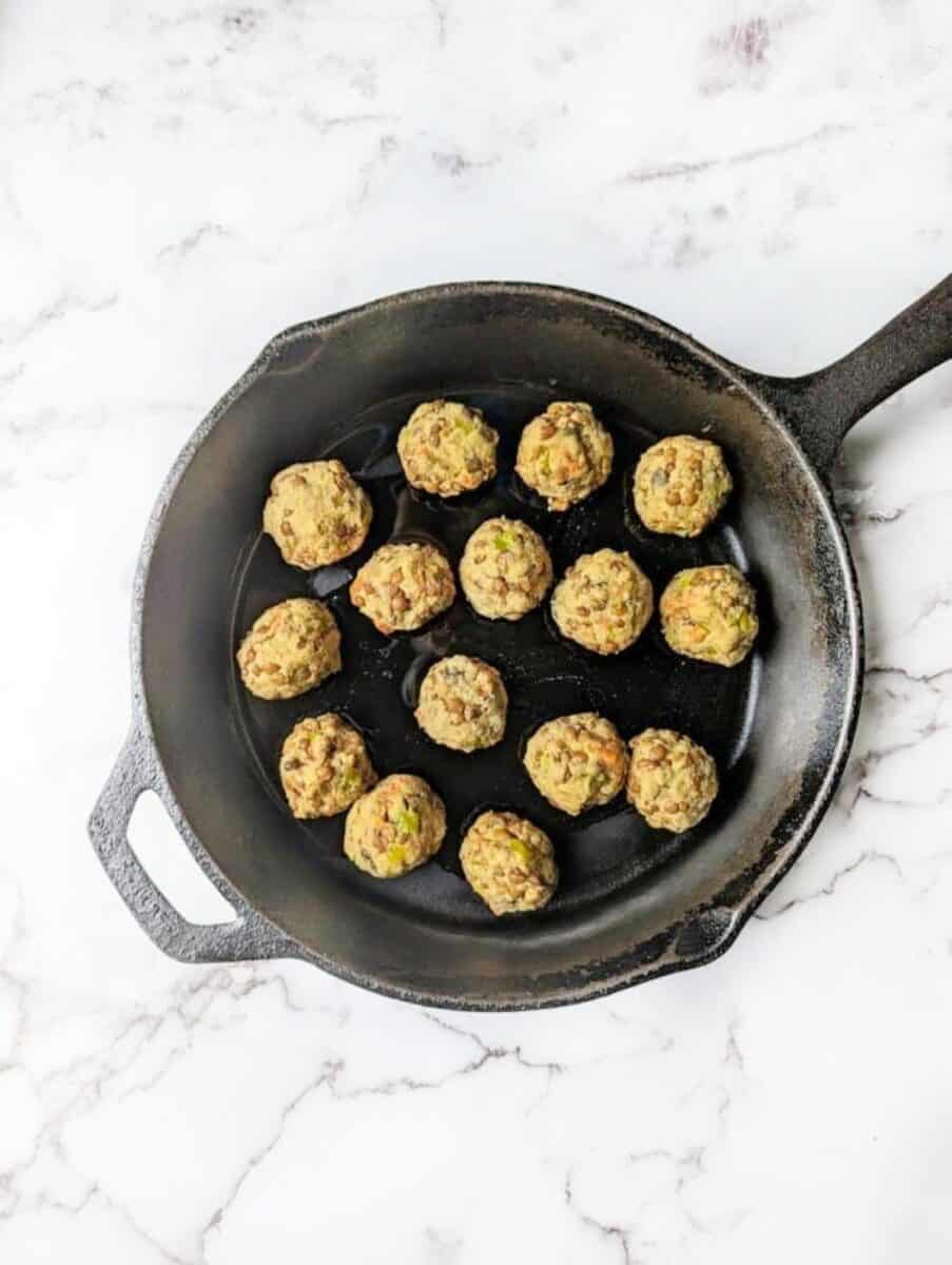 Super crispy vegan lentil balls fried slightly in a black skillet pan.