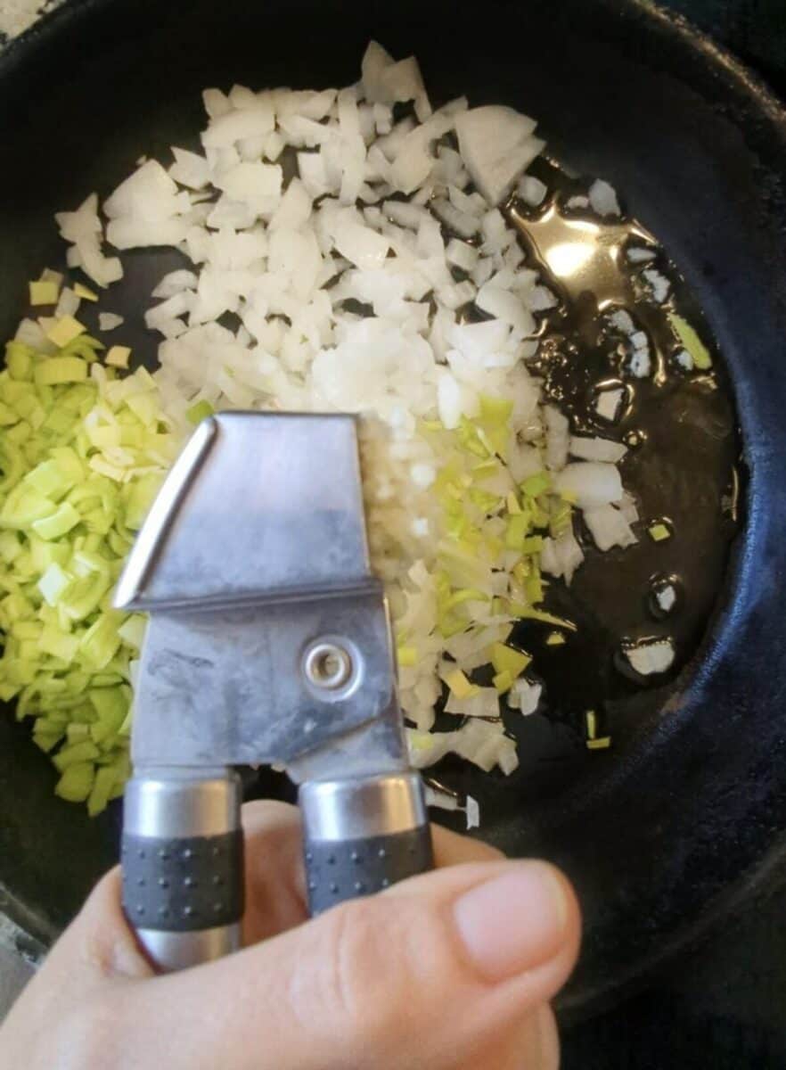 Sautéing chopped onions and garlic in a black skillet.