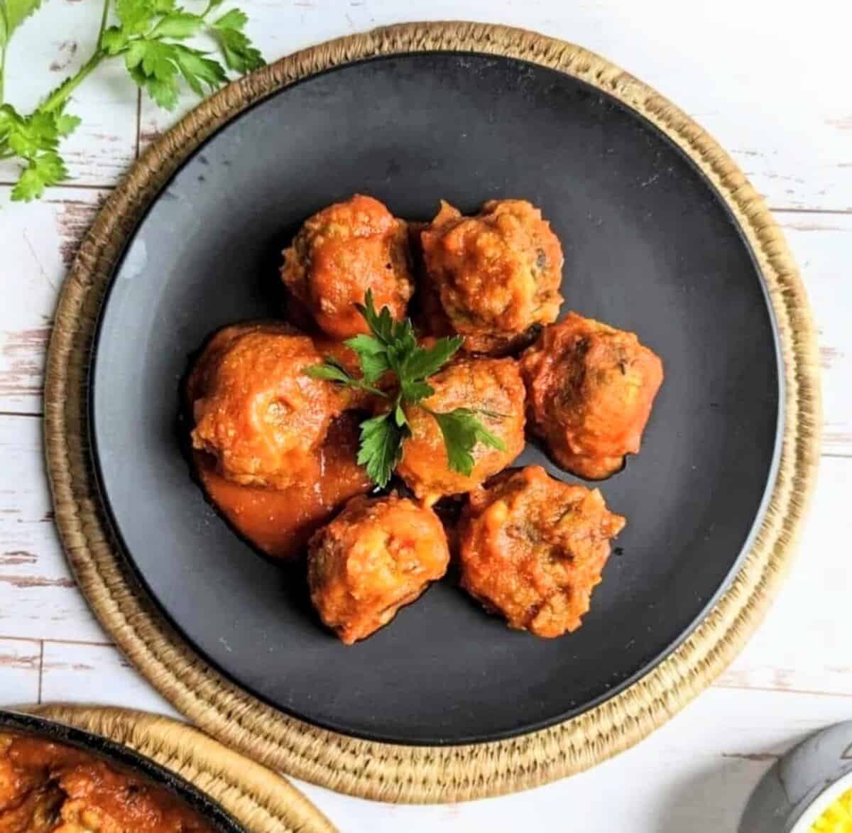 Vegan tomato lentil meatballs served on a black plate with fresh parsley garnish.