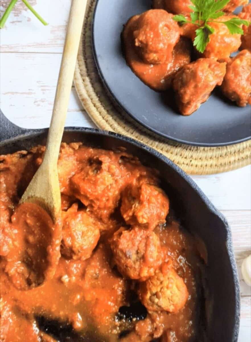 Creamy, flavorful vegan lentil meatballs meatballs in a spicy tomato sauce served in a skillet and on a plate.