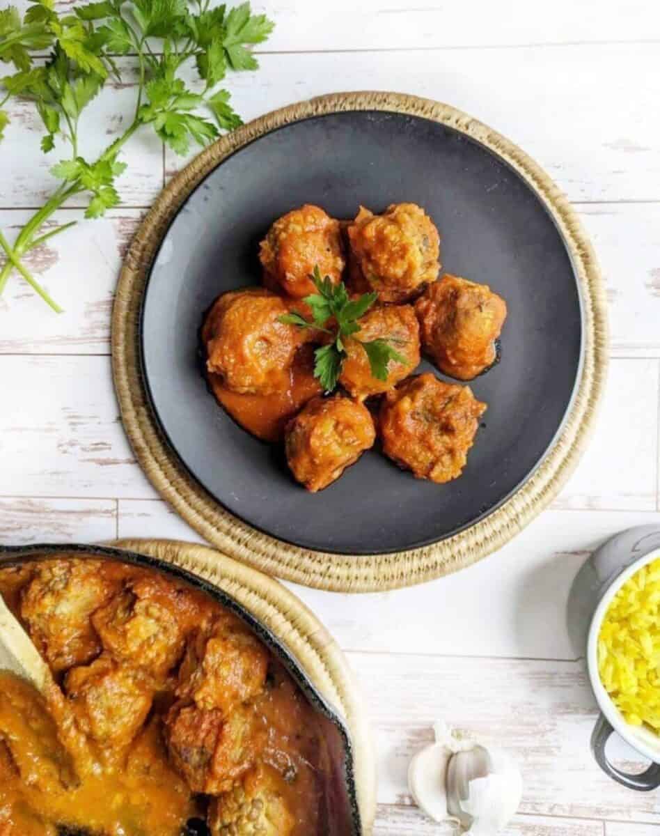 Vegan lentil meatballs served on a black plate with fresh parsley garnish. Cooked rice by the side.