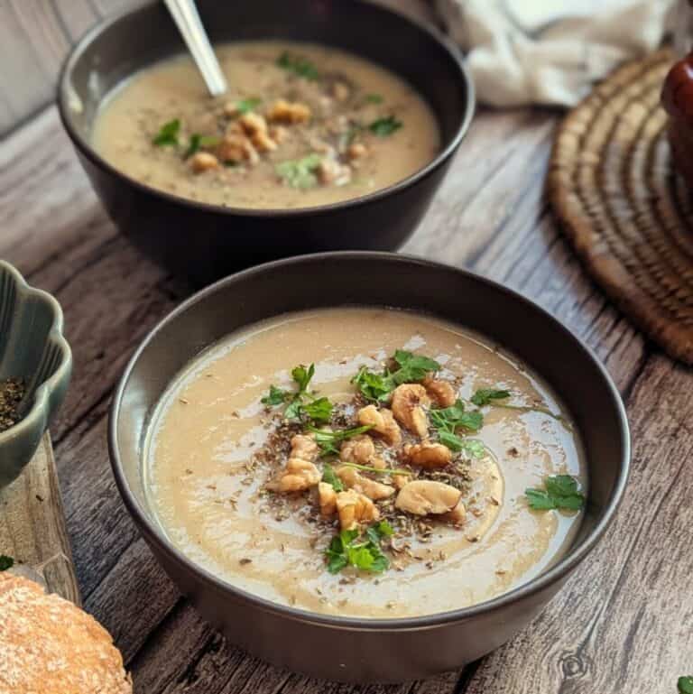 Two bowls of creamy potato cauliflower soup in a bowl with bread on the side.