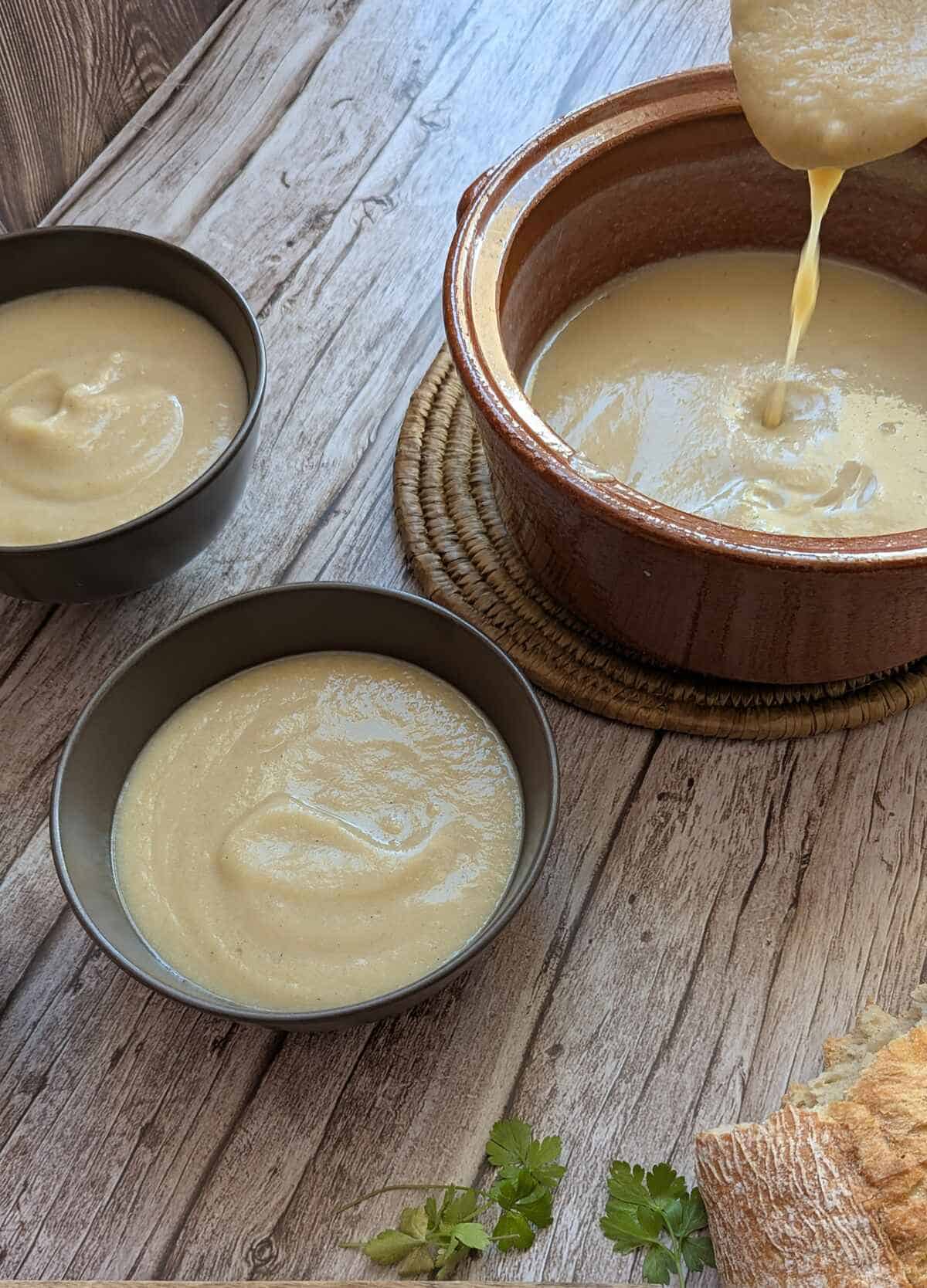 Creamy potato cauliflower soup being served in bowls on a rustic table.