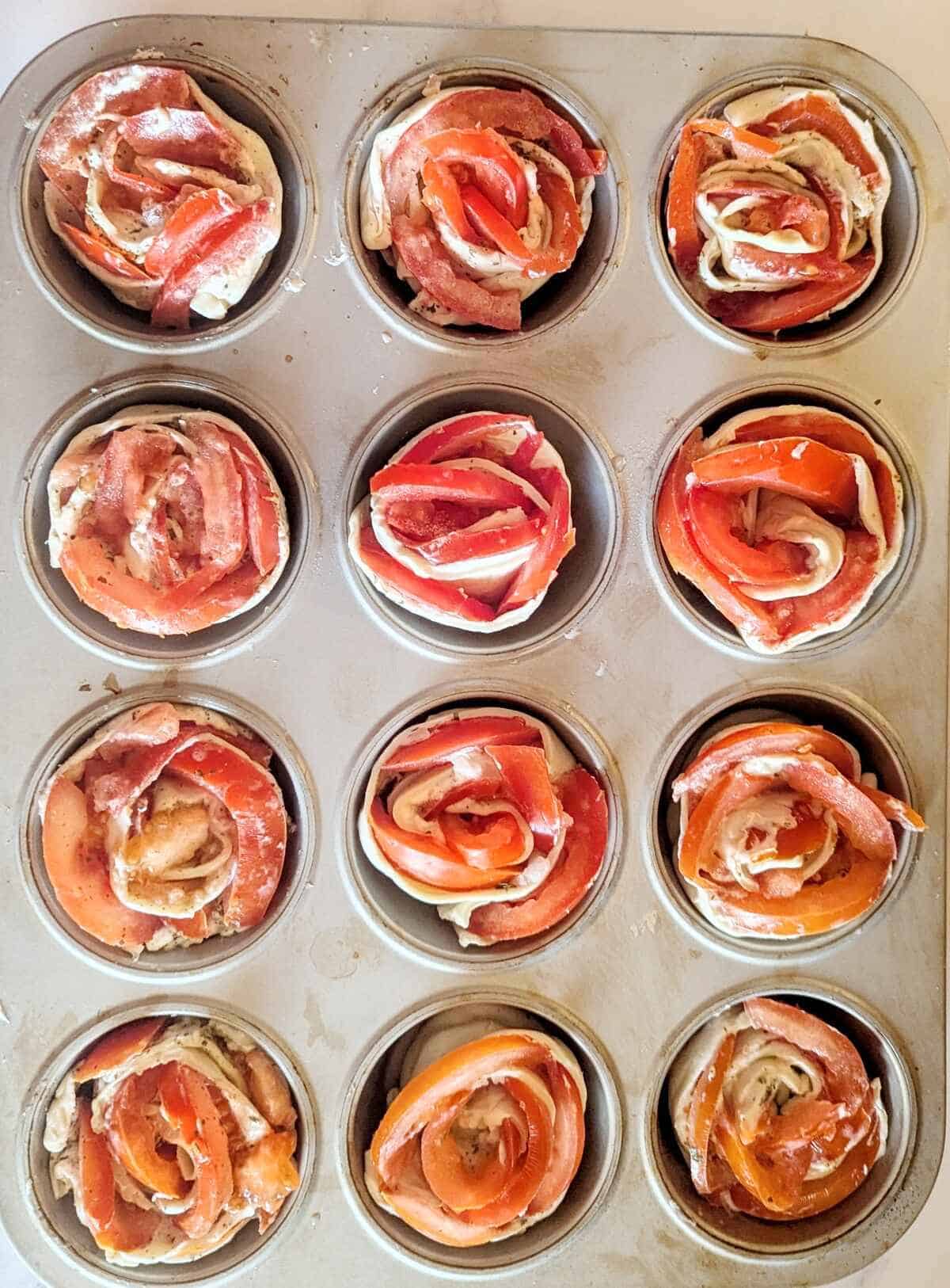 Crispy puff pastry tomato roses arranged in a greased muffin tin before baking.