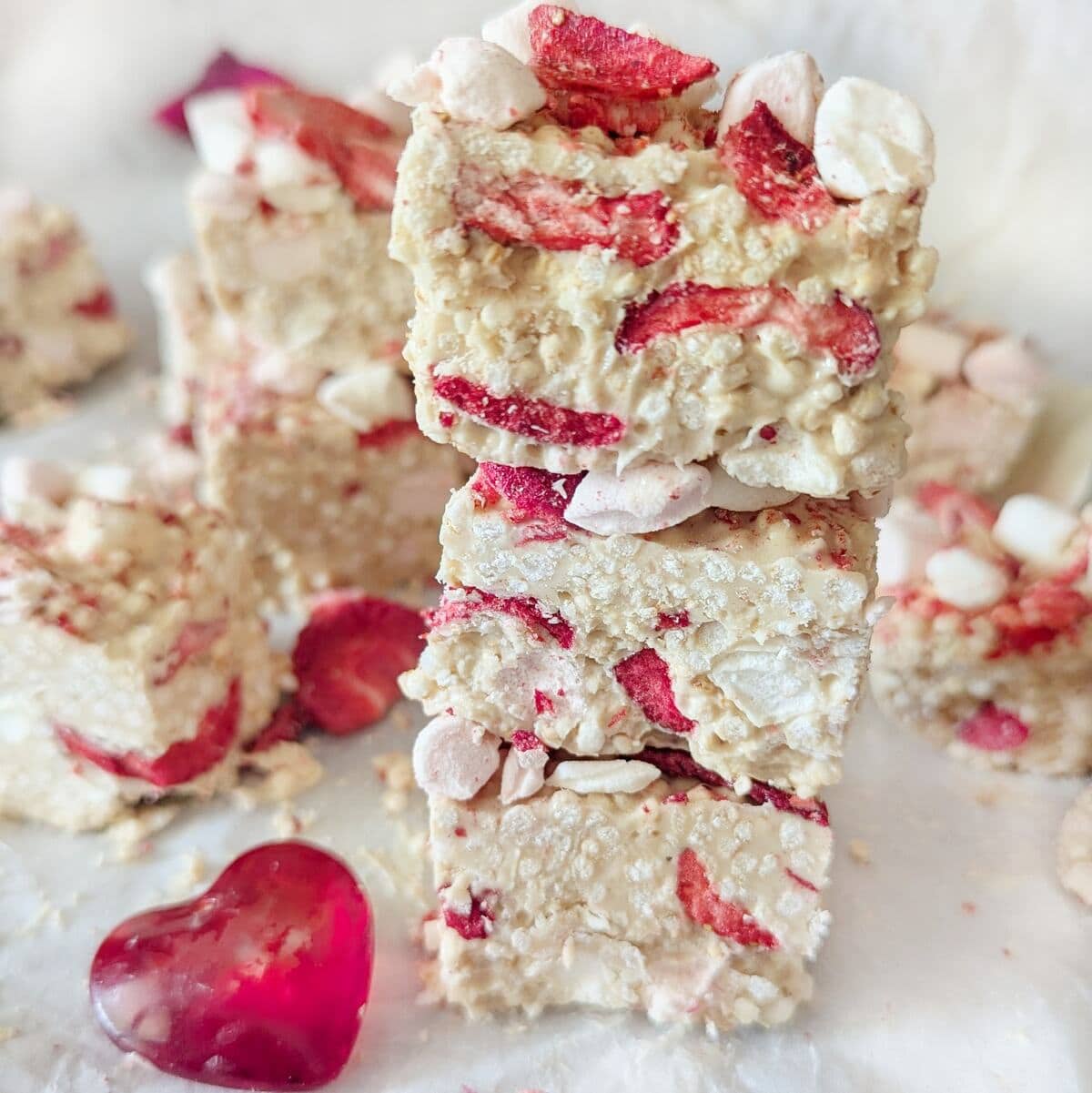 A close up white chocolate strawberry quinoa bites, stacked on top of each other. A glass love heart infront.
