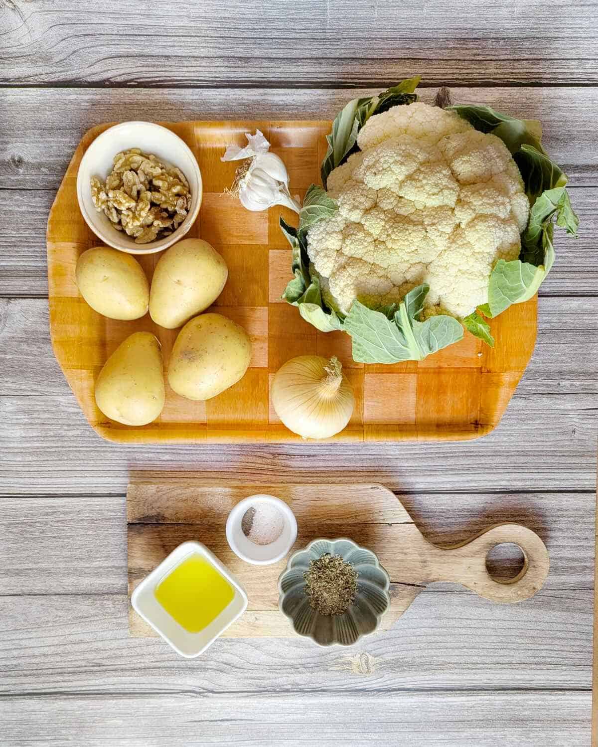 Ingredients for potato cauliflower soup on a tray: cauliflower, potatoes, garlic, onion, oregano, walnuts, oil, salt and pepper.