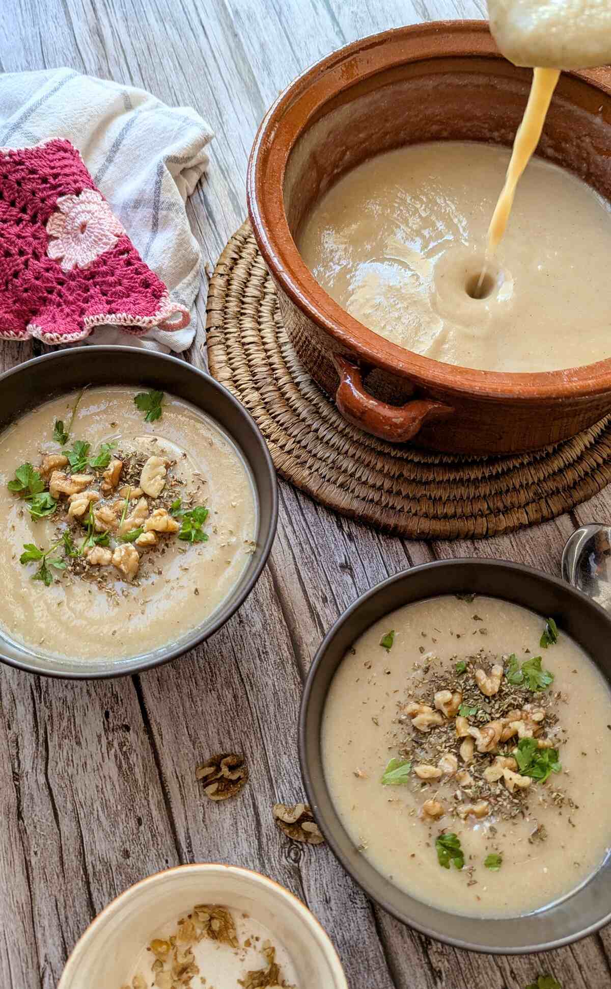 A serving bowl of soup with two dishes of creamy potato cauliflower soup on a rustic table.