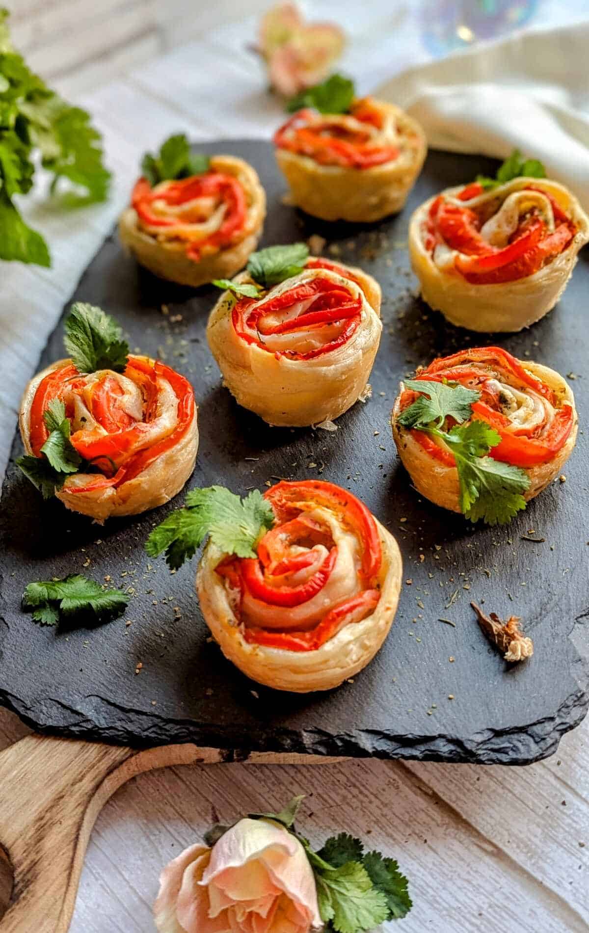 Puff pastry tomato roses displayed on a black tray with floral decoration.