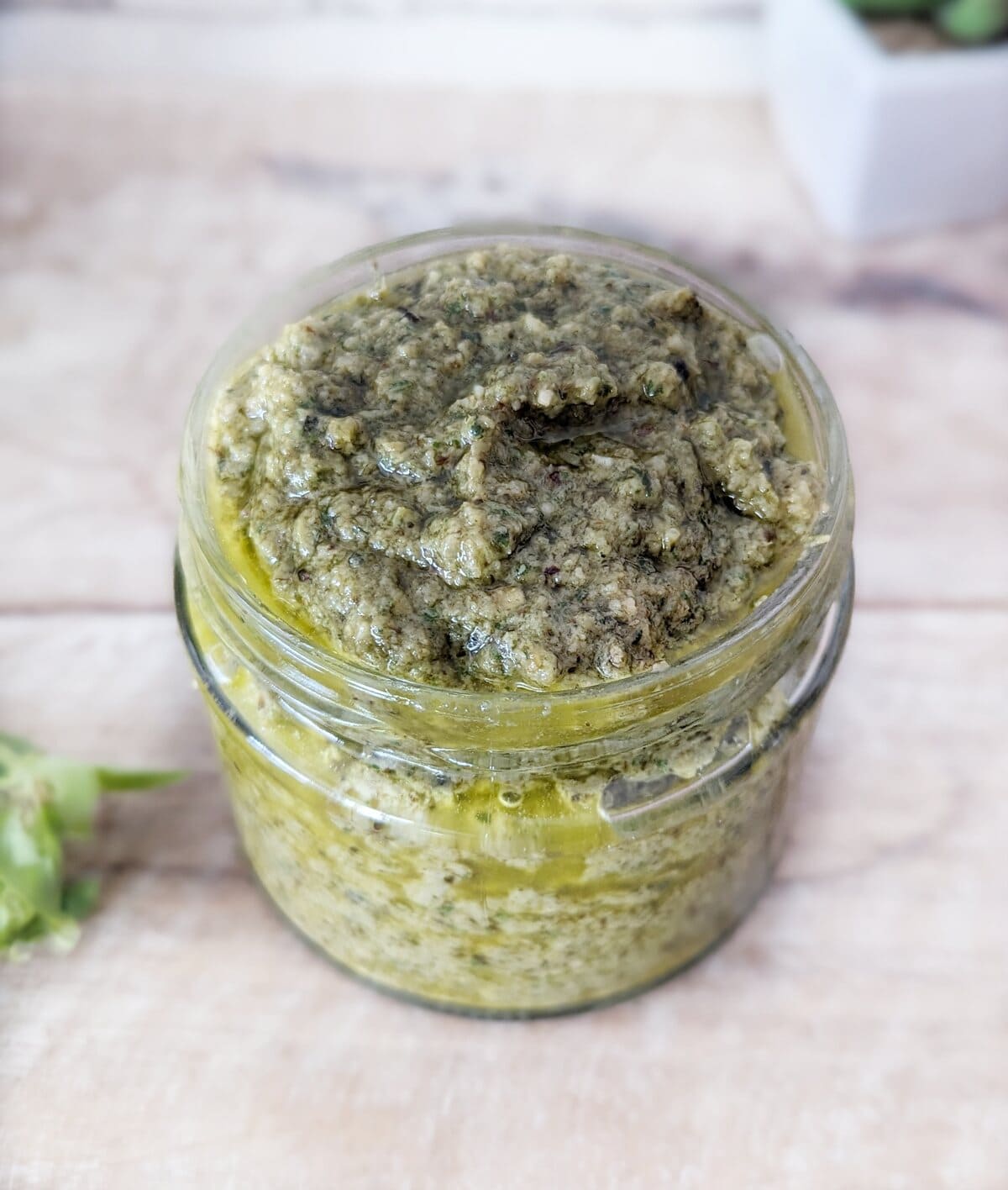 A glass pot of black garlic vegan pesto sitting on a white surface.