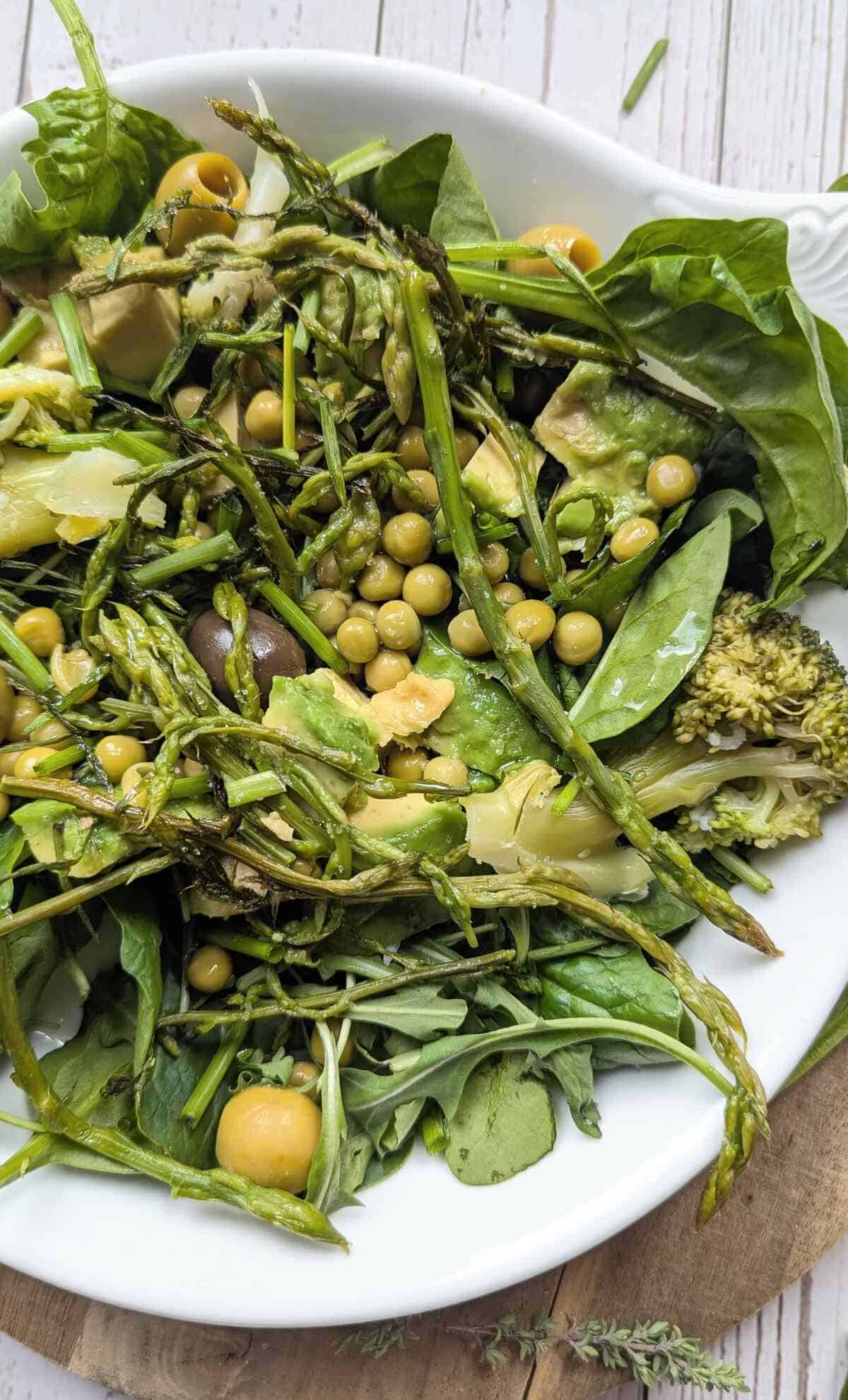A plate of assorted fresh vegetables and herbs including spinach, avocado, peas, and broccoli.