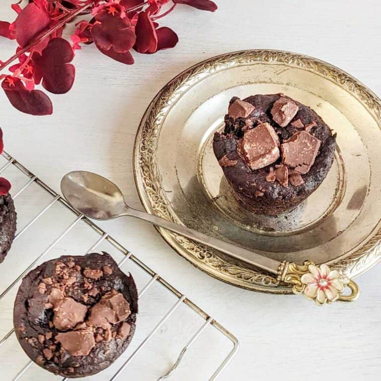 A chocolate banana muffin on a vintage plate and another on a cooking rack.