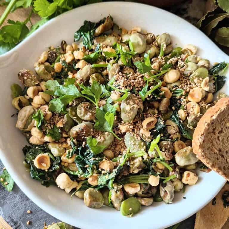 A plate of sautéed spinach and fava bean, with bread on the edge of the plate.