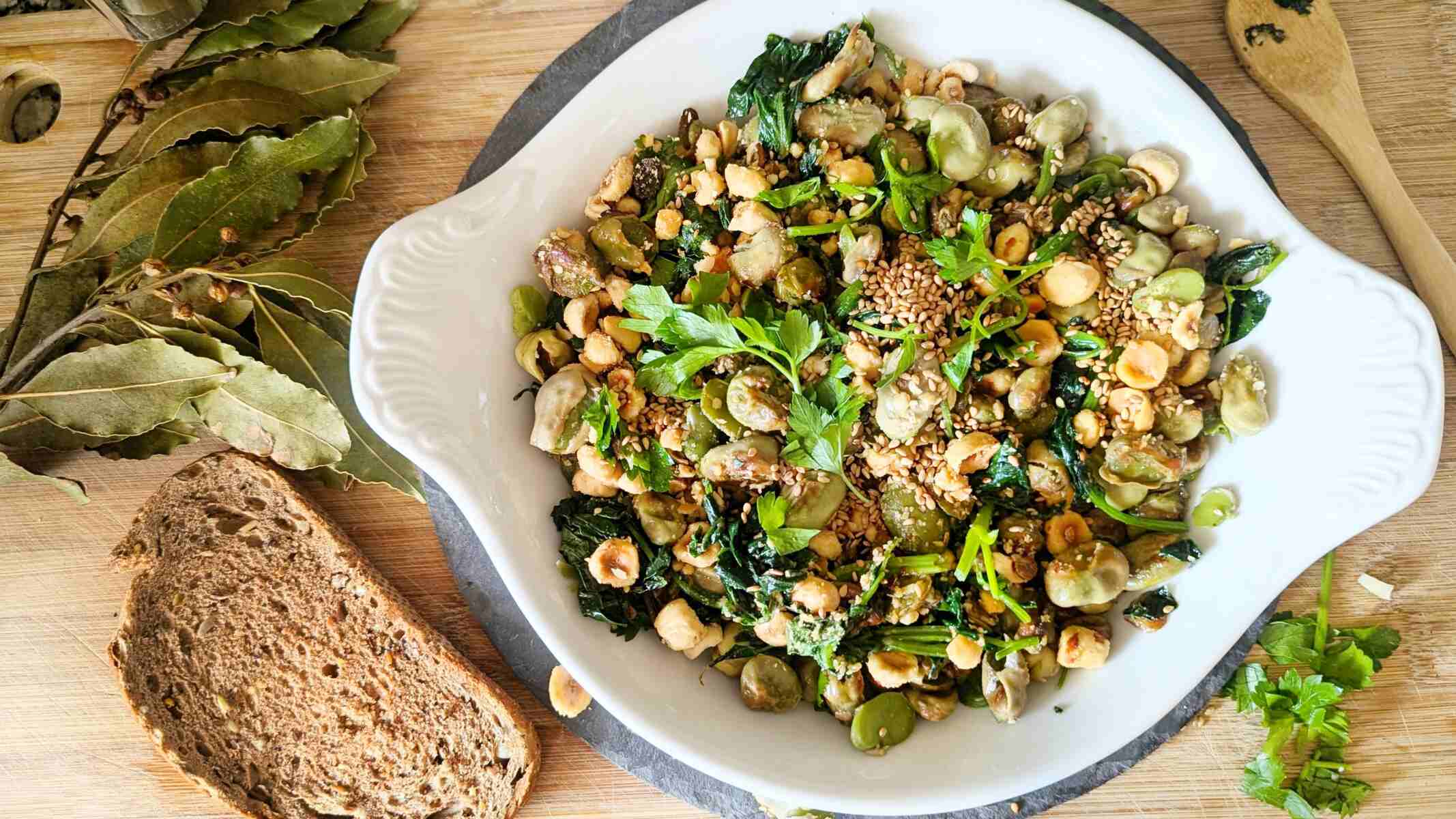 A dish of greens and broad beans. A slice of bread and bay leaves are by the side.