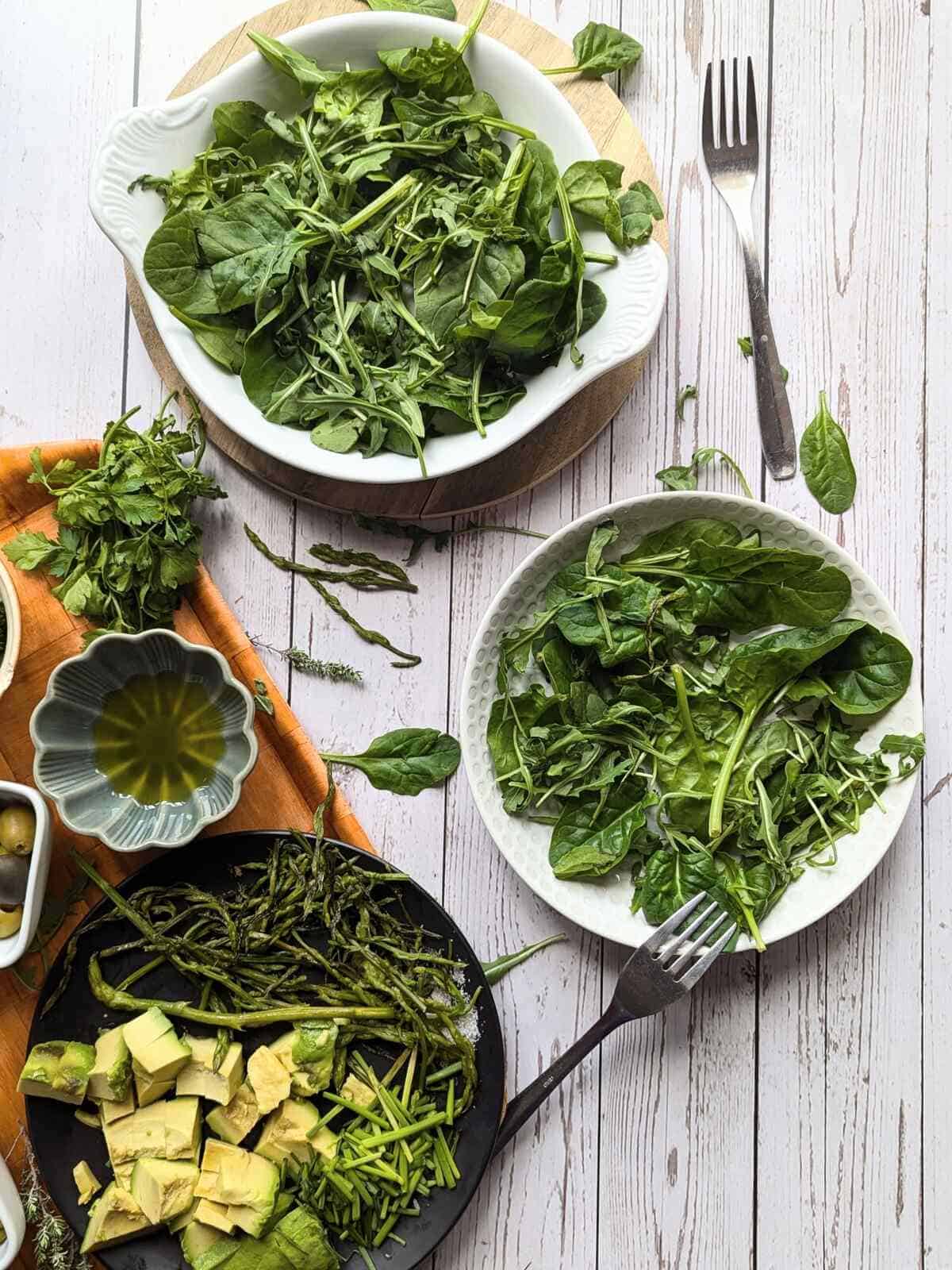 Assorted fresh leafy greens, wild asparagus, avocado, olives, peas and brocoli on white plates,